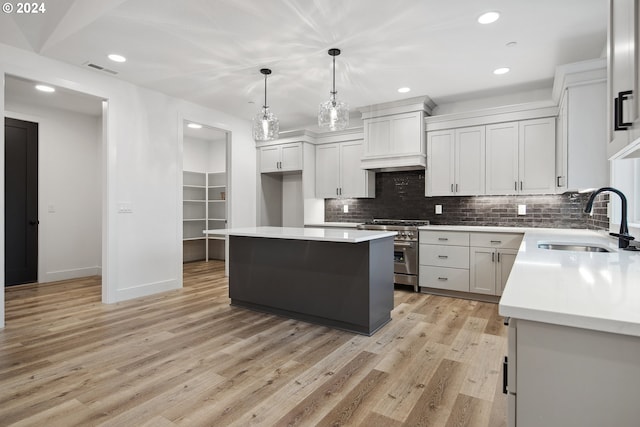 kitchen with high end range, sink, a kitchen island, decorative light fixtures, and light hardwood / wood-style floors