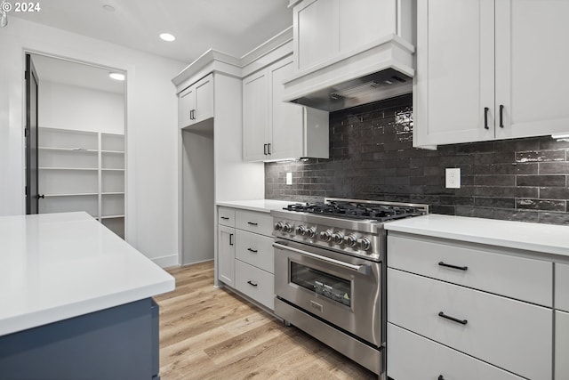 kitchen featuring custom exhaust hood, high end range, decorative backsplash, light wood-type flooring, and white cabinetry