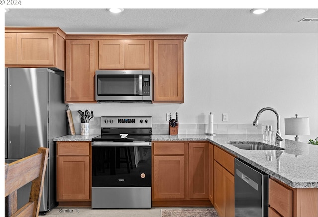 kitchen with visible vents, light stone countertops, a peninsula, stainless steel appliances, and a sink