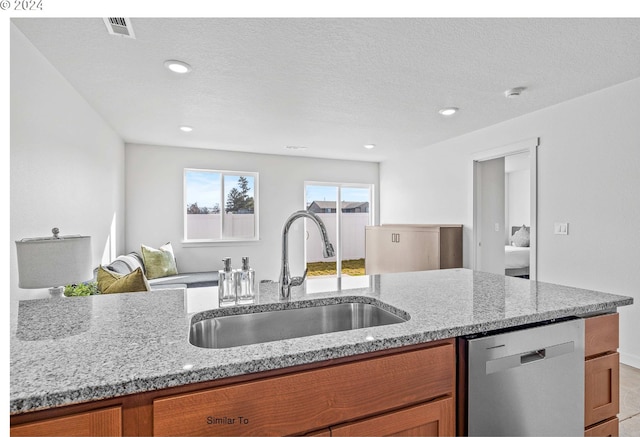 kitchen with stainless steel dishwasher, brown cabinetry, light stone countertops, and a sink