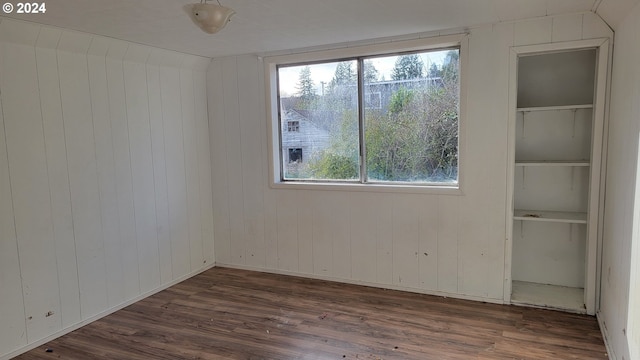 empty room with a healthy amount of sunlight, built in features, dark wood-type flooring, and wooden walls