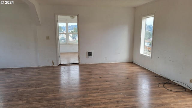 spare room featuring heating unit, plenty of natural light, and dark wood-type flooring