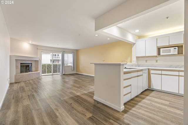 kitchen with kitchen peninsula, white cabinetry, light hardwood / wood-style floors, and white appliances