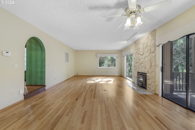 unfurnished living room with light hardwood / wood-style flooring, a textured ceiling, a wood stove, and ceiling fan