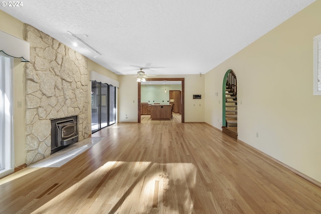 unfurnished living room featuring light wood-type flooring, a wood stove, a textured ceiling, rail lighting, and ceiling fan