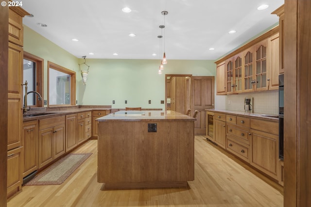 kitchen featuring a kitchen island with sink, electric stovetop, sink, pendant lighting, and light wood-type flooring