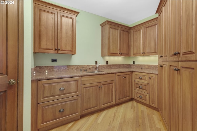 kitchen with light hardwood / wood-style floors, light stone countertops, and sink