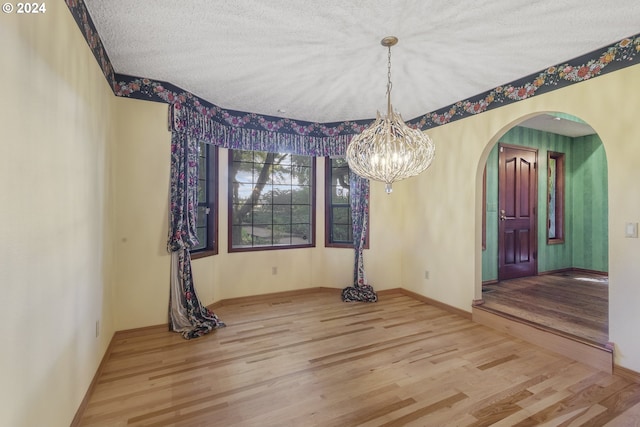 unfurnished dining area featuring wood-type flooring, a textured ceiling, and a chandelier