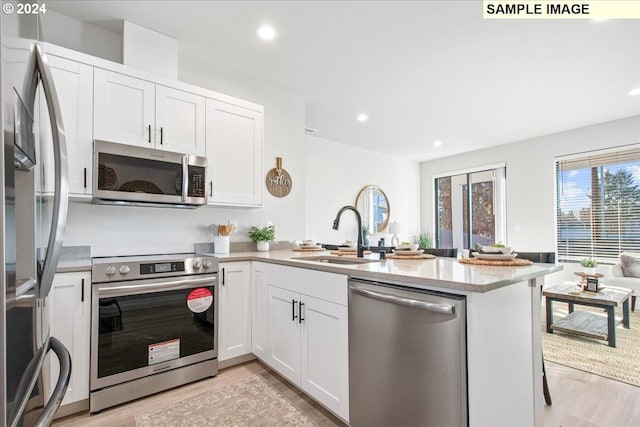 kitchen with white cabinets, light hardwood / wood-style floors, kitchen peninsula, and appliances with stainless steel finishes