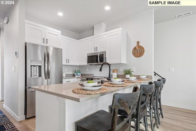 kitchen with light stone counters, light hardwood / wood-style floors, a breakfast bar, white cabinets, and appliances with stainless steel finishes