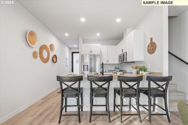 kitchen featuring a breakfast bar, sink, light hardwood / wood-style flooring, appliances with stainless steel finishes, and white cabinetry