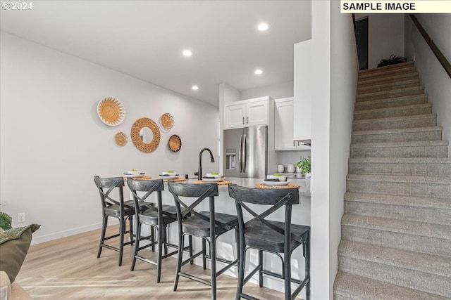 kitchen featuring stainless steel fridge with ice dispenser, kitchen peninsula, a breakfast bar area, white cabinets, and light wood-type flooring