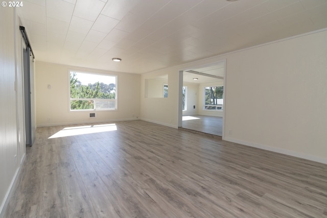 unfurnished room with plenty of natural light, a barn door, baseboards, and wood finished floors