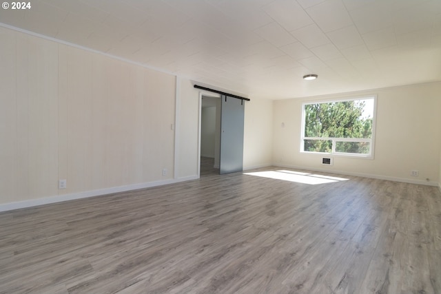 unfurnished room with wood finished floors, baseboards, and a barn door