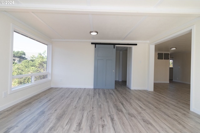 empty room with a barn door, ornamental molding, and light hardwood / wood-style flooring