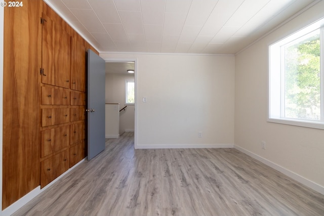 empty room featuring light wood-style flooring, baseboards, and ornamental molding