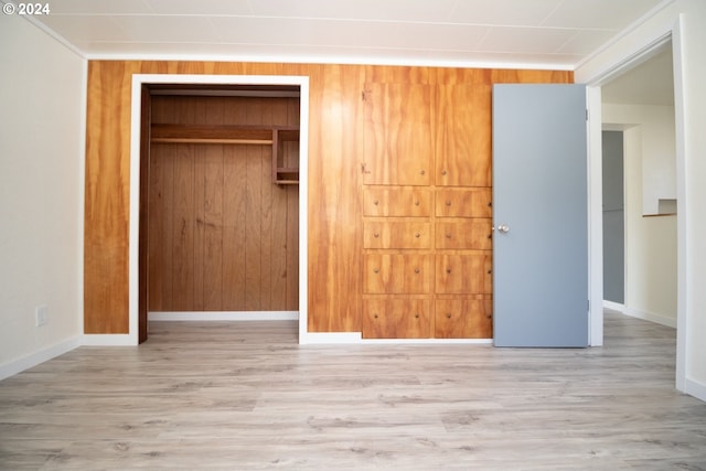 unfurnished bedroom with a closet, wood finished floors, baseboards, and wooden walls