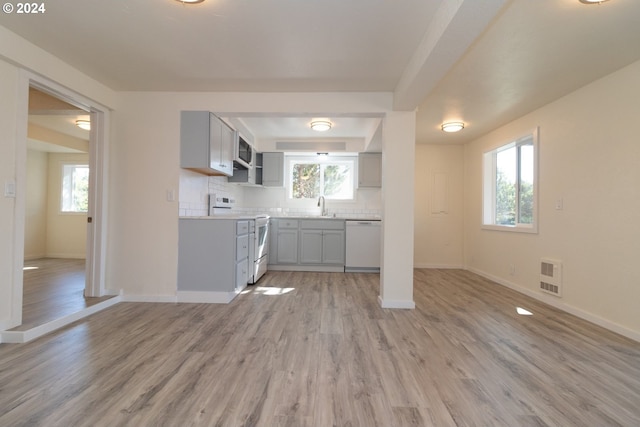 kitchen featuring tasteful backsplash, baseboards, a sink, white appliances, and light wood finished floors