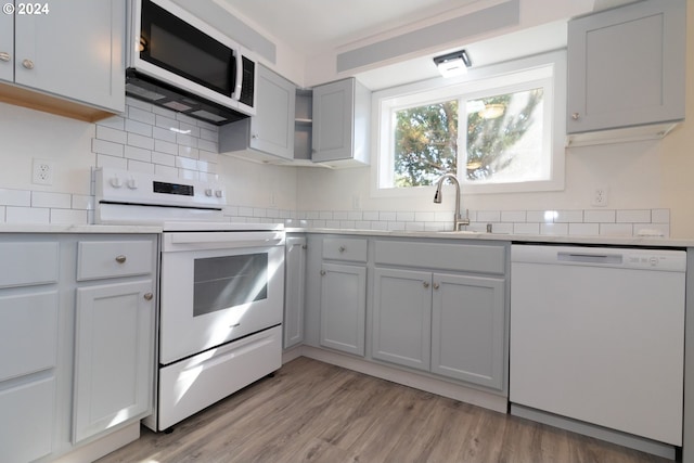 kitchen featuring light wood-type flooring, gray cabinets, white appliances, light countertops, and a sink