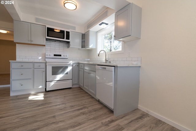kitchen featuring a sink, gray cabinets, light wood finished floors, and white appliances