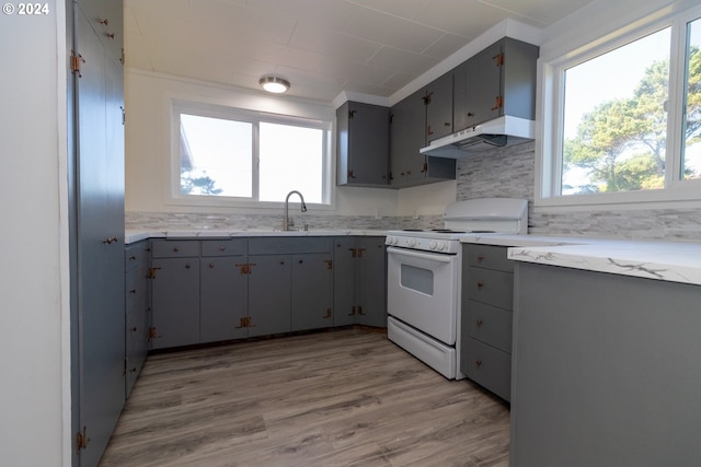 kitchen featuring gas range gas stove, light wood-style floors, under cabinet range hood, gray cabinetry, and backsplash