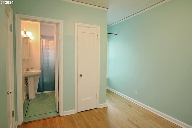 unfurnished bedroom featuring sink, ensuite bath, ornamental molding, and light wood-type flooring