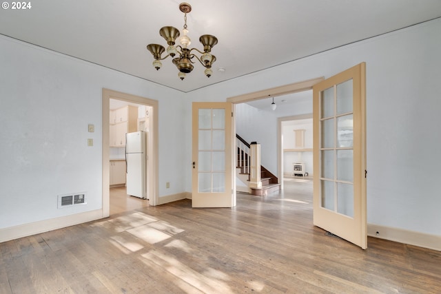 spare room featuring an inviting chandelier, hardwood / wood-style floors, and french doors