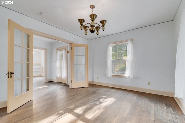 empty room featuring french doors, a notable chandelier, and hardwood / wood-style flooring