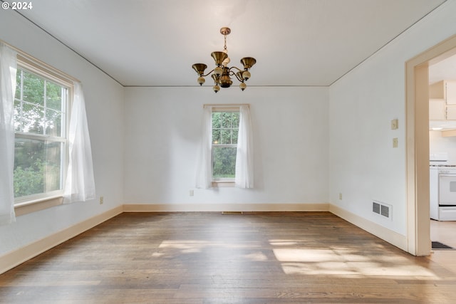 empty room with an inviting chandelier, wood-type flooring, and plenty of natural light