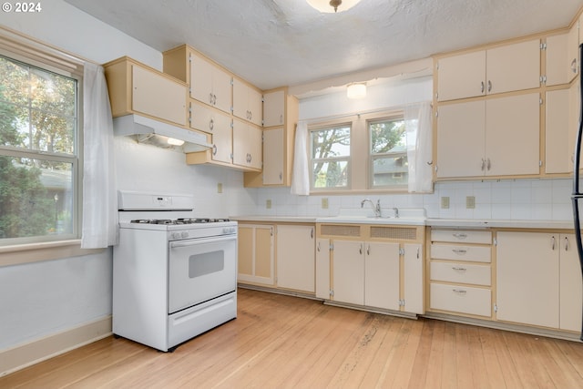 kitchen featuring white range with gas cooktop, sink, light wood-type flooring, and decorative backsplash