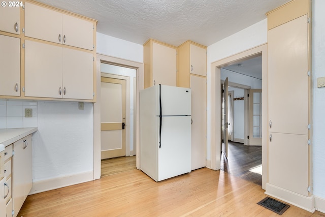 kitchen featuring white refrigerator, white cabinets, a textured ceiling, and light hardwood / wood-style flooring