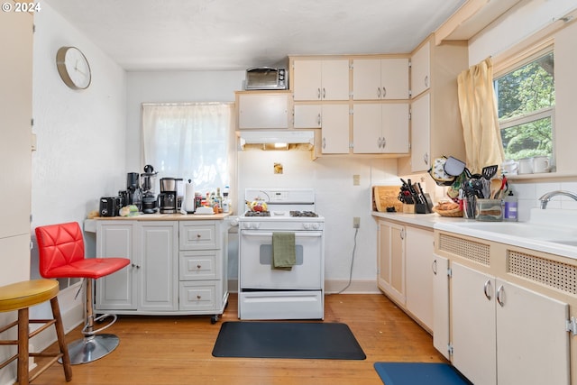 kitchen with light hardwood / wood-style floors, white gas range oven, and white cabinets