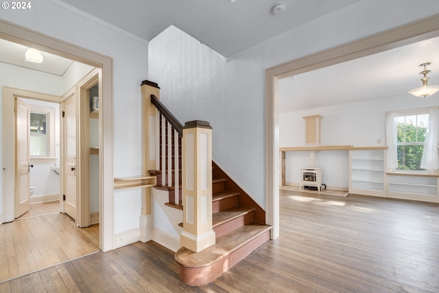 staircase with crown molding, wood-type flooring, and a wood stove