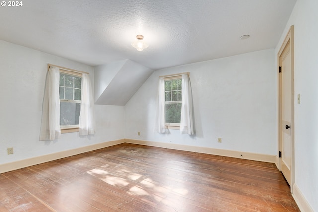 additional living space featuring hardwood / wood-style flooring, vaulted ceiling, and a textured ceiling