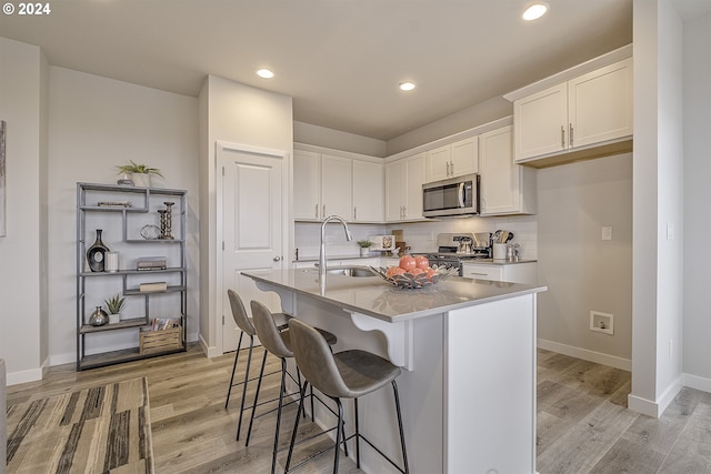 kitchen featuring a breakfast bar, white cabinetry, an island with sink, sink, and stainless steel appliances