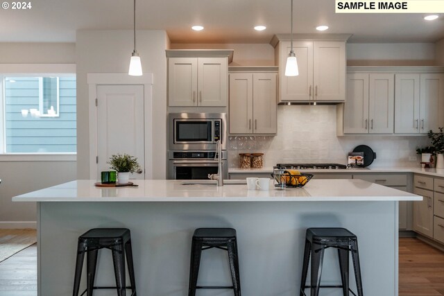 kitchen with a breakfast bar, backsplash, a kitchen island with sink, wood-type flooring, and stainless steel appliances