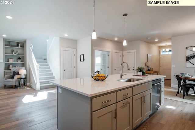 kitchen featuring dishwashing machine, sink, a kitchen island with sink, gray cabinetry, and decorative light fixtures