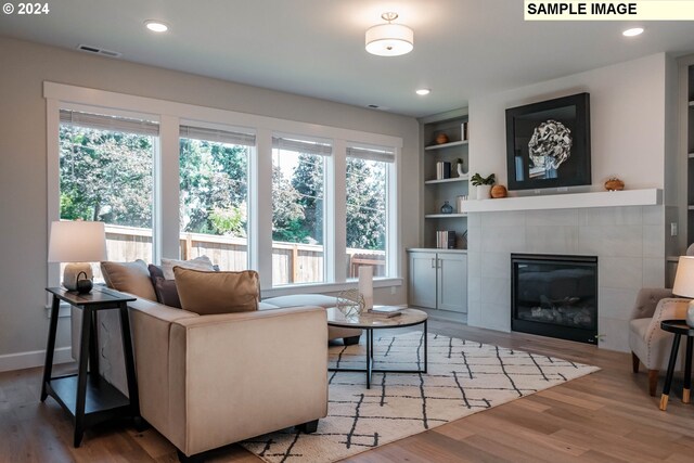 living room with a tiled fireplace, built in features, and hardwood / wood-style flooring