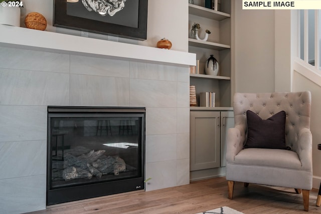 living area with light hardwood / wood-style floors, built in features, and a tile fireplace