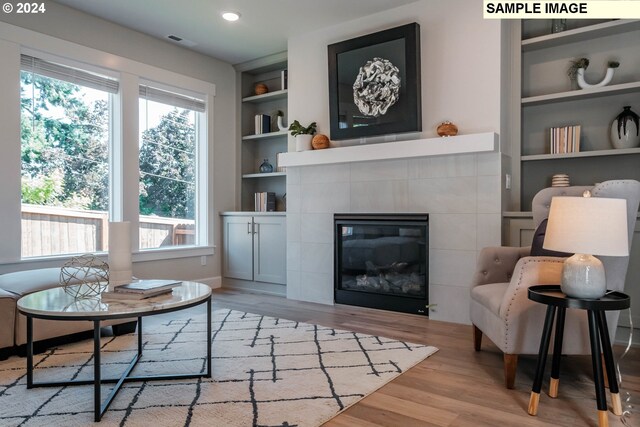 sitting room featuring a tiled fireplace, built in features, and light wood-type flooring