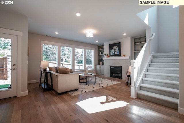 living room with a tiled fireplace, built in features, and light hardwood / wood-style flooring