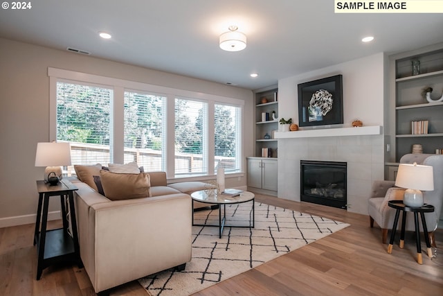 living room featuring a tiled fireplace, a wealth of natural light, light hardwood / wood-style flooring, and built in shelves