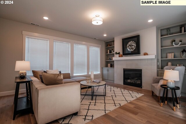 living room featuring hardwood / wood-style flooring, built in features, and a tiled fireplace