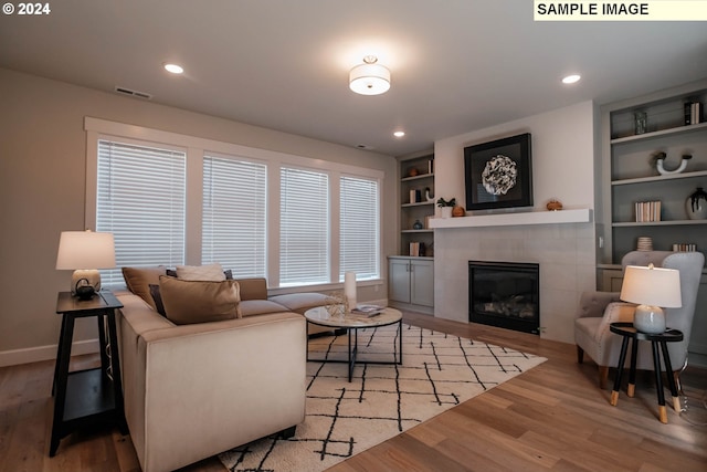 living room with wood-type flooring, a tiled fireplace, and built in features