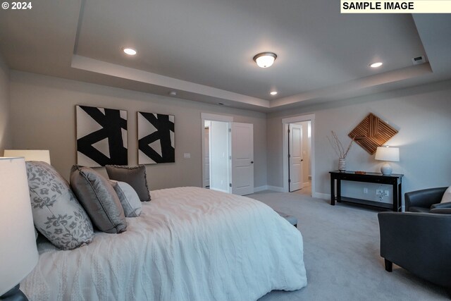 bedroom featuring light carpet, ensuite bathroom, and a raised ceiling