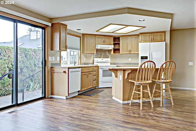 kitchen featuring hardwood / wood-style flooring, sink, a center island, white appliances, and tasteful backsplash