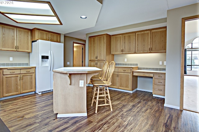 kitchen with dark hardwood / wood-style floors, white fridge with ice dispenser, a breakfast bar, and a kitchen island