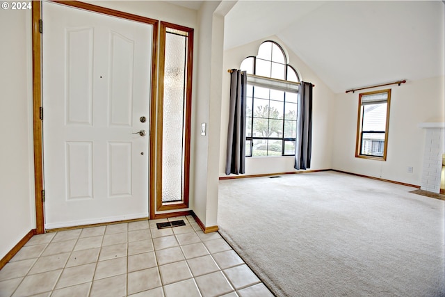 foyer entrance featuring lofted ceiling, light colored carpet, and a brick fireplace