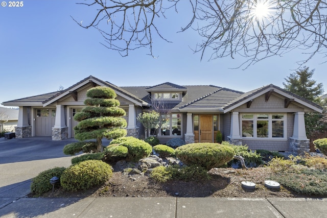 craftsman inspired home with stone siding, a tile roof, and concrete driveway