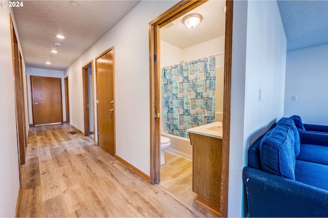 hall featuring light wood-type flooring and a textured ceiling